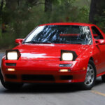 Red Mazda RX7 FC on road with trees in background