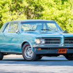 light blue Pontiac in front of trees