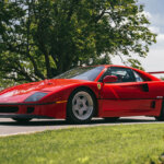Red Ferrari F40 parked on street with grass and roses in front of it