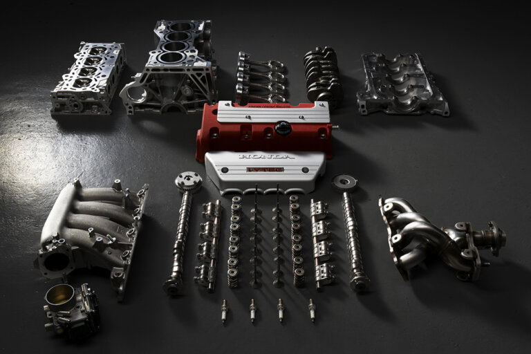 Engine parts layed out on a dark concrete floor. Metal cam shafts, manifolds, pistons, next to red valve cover