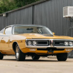 yellow with black racing stripes 1970 dodge charger parked in front of building