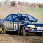 mcrae in a blue subaru impreza rally car on a dirt road