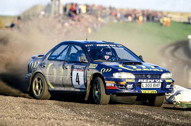 mcrae in a blue subaru impreza rally car on a dirt road