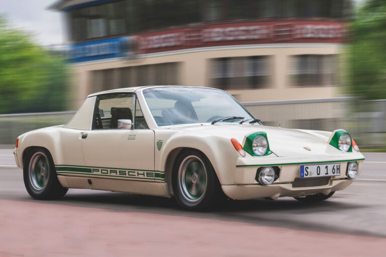 White with green trim Porsche 914 driving on a road passing a building