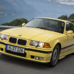 yellow e36 m3 driving on a country road
