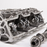 Engine block opened up with camshaft laying flat next to it on white background