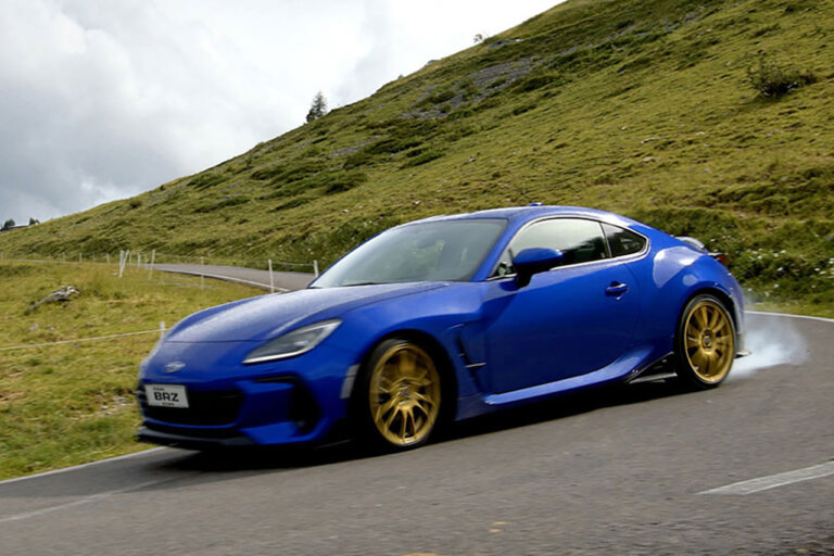 Blue BRZ Touge Edition with gold wheels drifting through a turn with a grassy mountain in the background