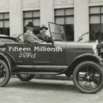 Henry Ford and Edsel Ford sitting in a Ford Model T that says Fifteenth Million Ford on the side of it