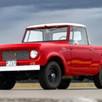 Red International Harvester Scout 80 truck parked on a road with cloudy skies behind it