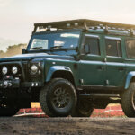 Green Land Rover Defender parked at an angle with the sun setting in background