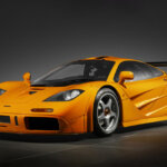 Orange McLaren F1 in a room with black tile floor and black background