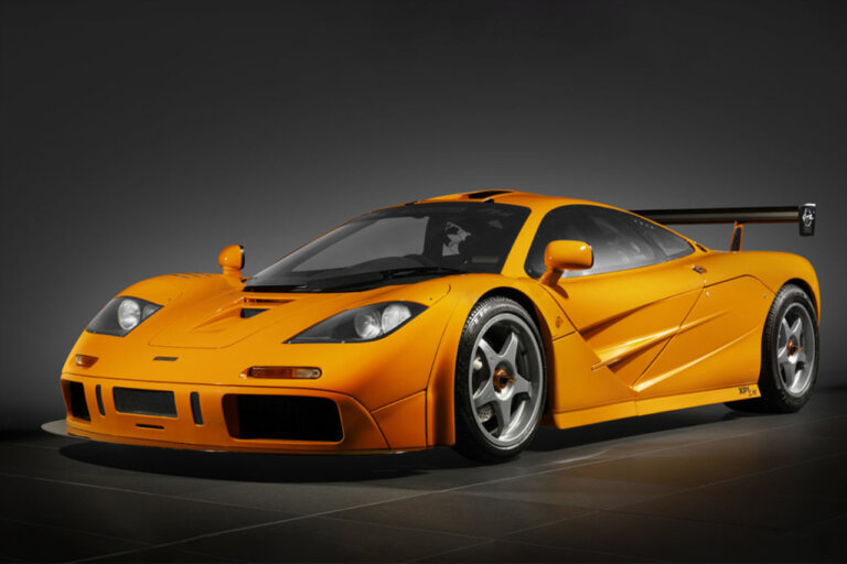 Orange McLaren F1 in a room with black tile floor and black background