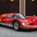 red Porsche 906 parked in a driveway in front of a garage