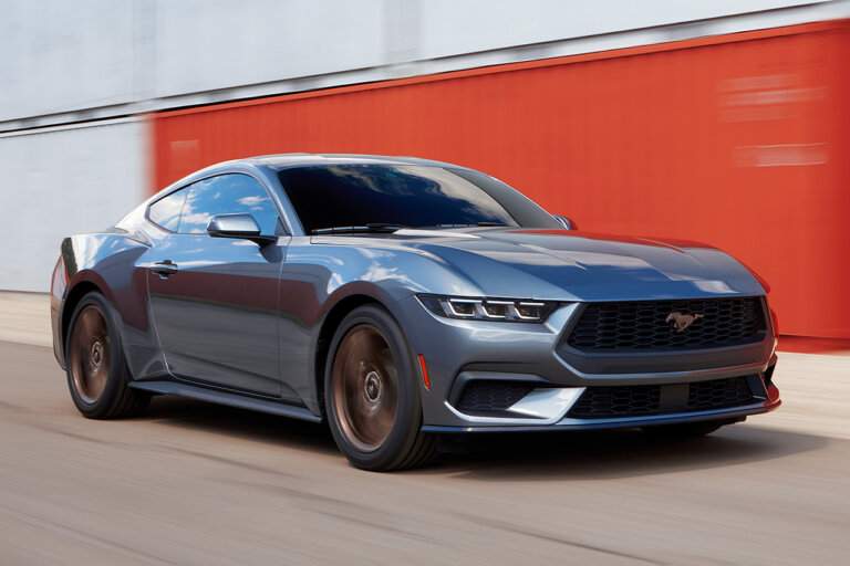 Grey 2024 Mustang GT driving past red shipping containers