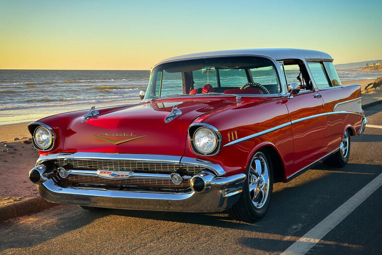 Red Chevy Nomad station wagon pictured on the side of a freeway with the ocean and sunset behind it