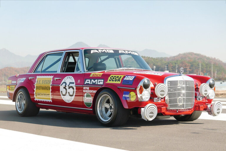 red modified Mercedes car on racetrack with many decals covering the car