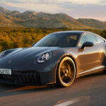 Grey Porsche 911 driving on road with mountain and trees in background