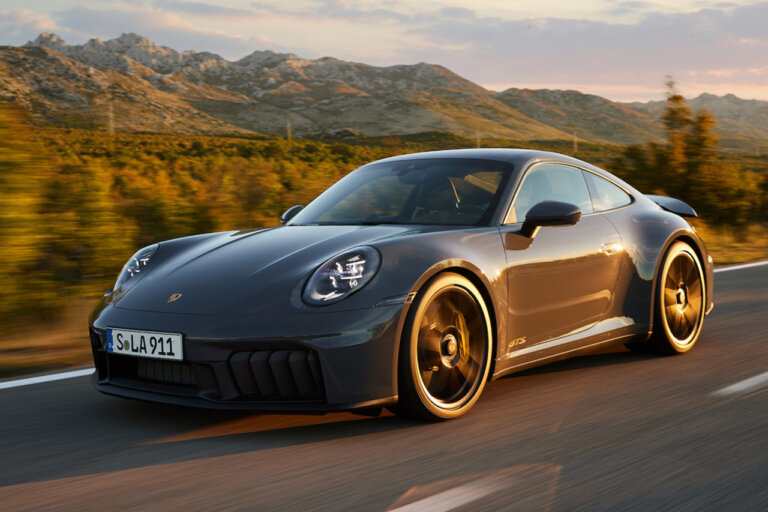 Grey Porsche 911 driving on road with mountain and trees in background