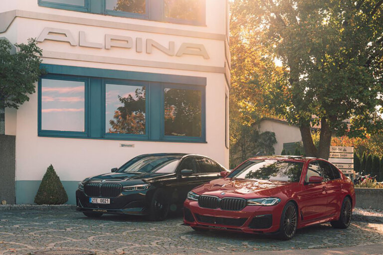 two bmw cars one blue one red next to each other in front of a store that says Alpina above it