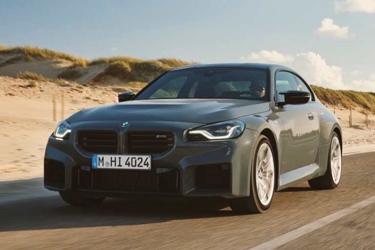 Grey BMW M2 driving down the freeway with sand and grass hills behind it