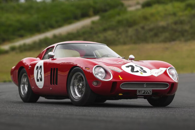 Red Ferrari 250 GTO parked on ground with grassy hill in background
