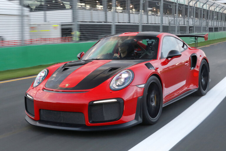 Red and black Porsche 911 GT2RS with a man driving on a race track with seats in background