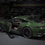 Green Porsche 911 pictured in a dark room with a sign above it