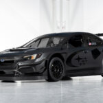 Black Subaru WRX with large rear spoiler pictured in a warehouse with white walls