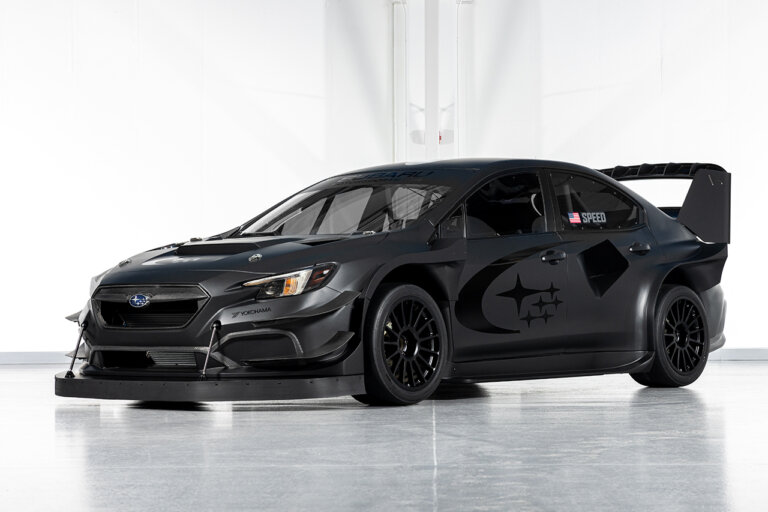 Black Subaru WRX with large rear spoiler pictured in a warehouse with white walls