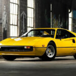 Yellow Ferrari 308 parked in a warehouse with large vertical windows in background