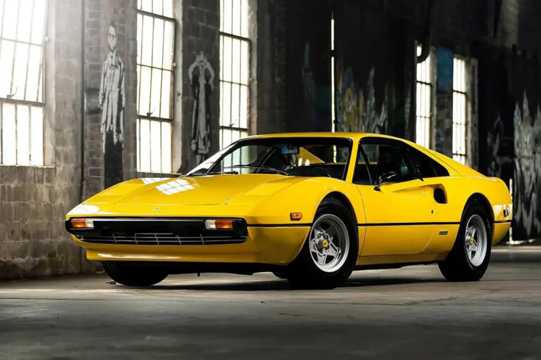 Yellow Ferrari 308 parked in a warehouse with large vertical windows in background