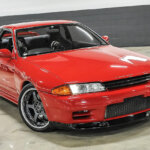 Red Nissan Skyline R32 parked in a white garage with grey brick in background