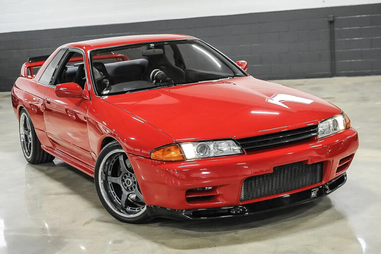 Red Nissan Skyline R32 parked in a white garage with grey brick in background