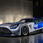 silver, blue Mercedes-Benz AMG GT3 parked in a dark room with a grey brick wall in the background