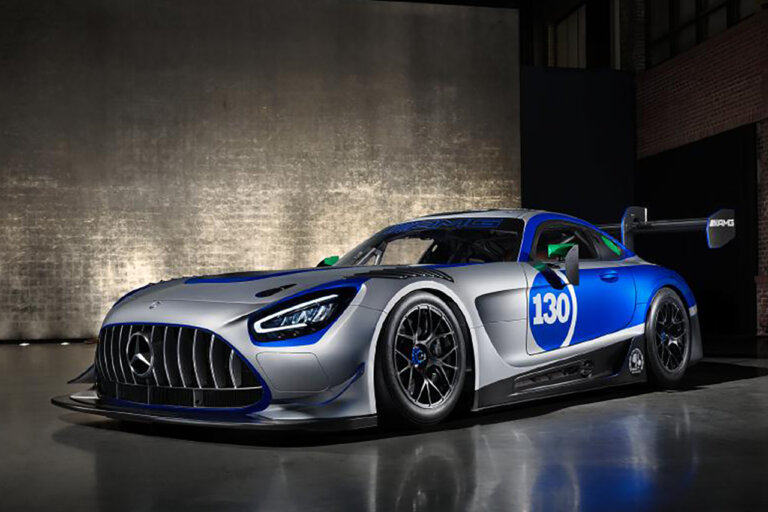 silver, blue Mercedes-Benz AMG GT3 parked in a dark room with a grey brick wall in the background