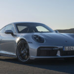 Silver Porsche car parked on the road with mountains and clear blue sky in background