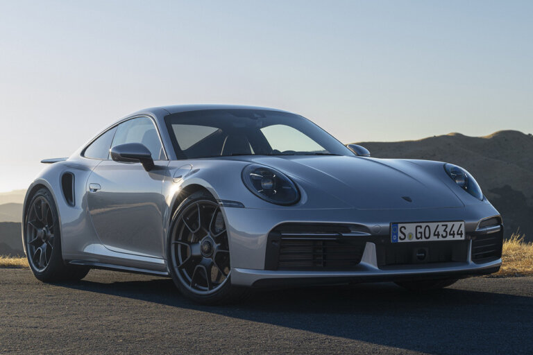 Silver Porsche car parked on the road with mountains and clear blue sky in background