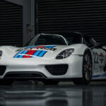 White Porsche 918 with red and blue stripes on hood in a dark room