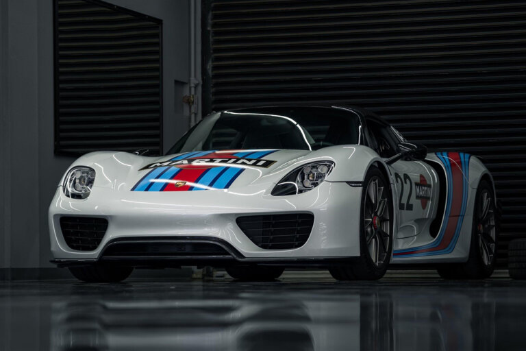 White Porsche 918 with red and blue stripes on hood in a dark room