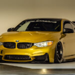 Gold BMW M4 parked in a studio with a white background
