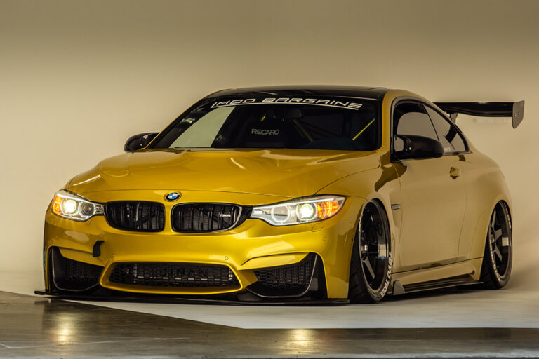 Gold BMW M4 parked in a studio with a white background