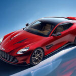 red Aston Martin car parked at an angle on a blue background with reflection of the car on the floor