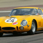 Yellow Ferrari 275 GTB on the race track driving fast through a turn
