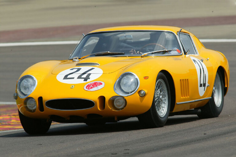 Yellow Ferrari 275 GTB on the race track driving fast through a turn