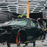 Green Porsche on wheel dollys with three people around the car under hexagon LED lights inside of a garage