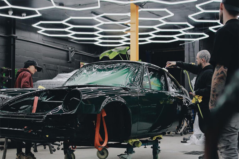 Green Porsche on wheel dollys with three people around the car under hexagon LED lights inside of a garage