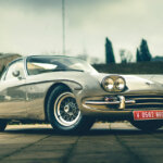 Silver Lamborghini 350 GT car parked on stone ground with trees and a building behind it