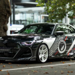 Black with red and white accents of a BMW m240i parked under a tree with leaves on the ground