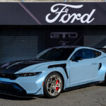 Blue Ford Mustang GTD parked in front of a store with the word Ford in white above it
