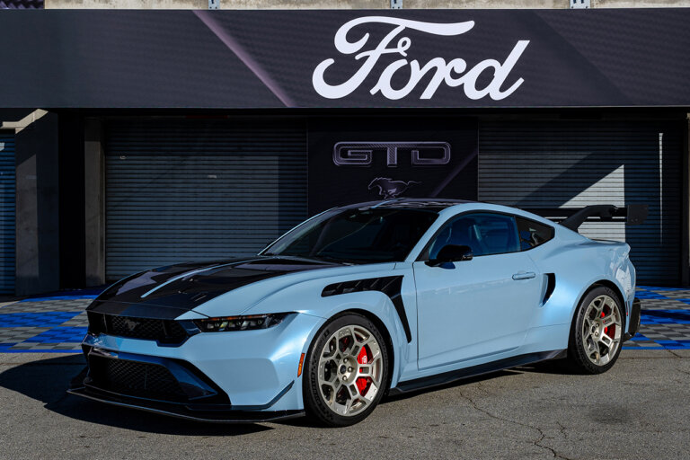 Blue Ford Mustang GTD parked in front of a store with the word Ford in white above it